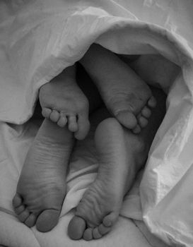 Close-up of intertwined feet under a blanket, capturing warmth and comfort.