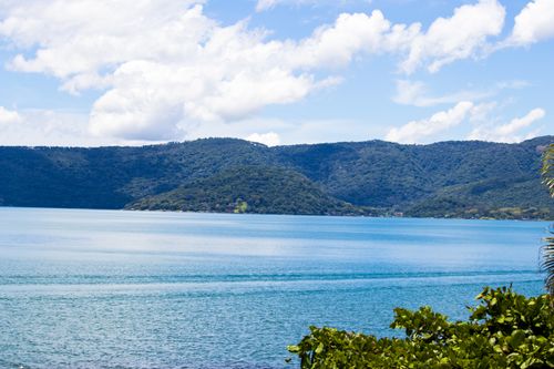 Free A picturesque lake with surrounding green hills under a vibrant summer sky. Stock Photo