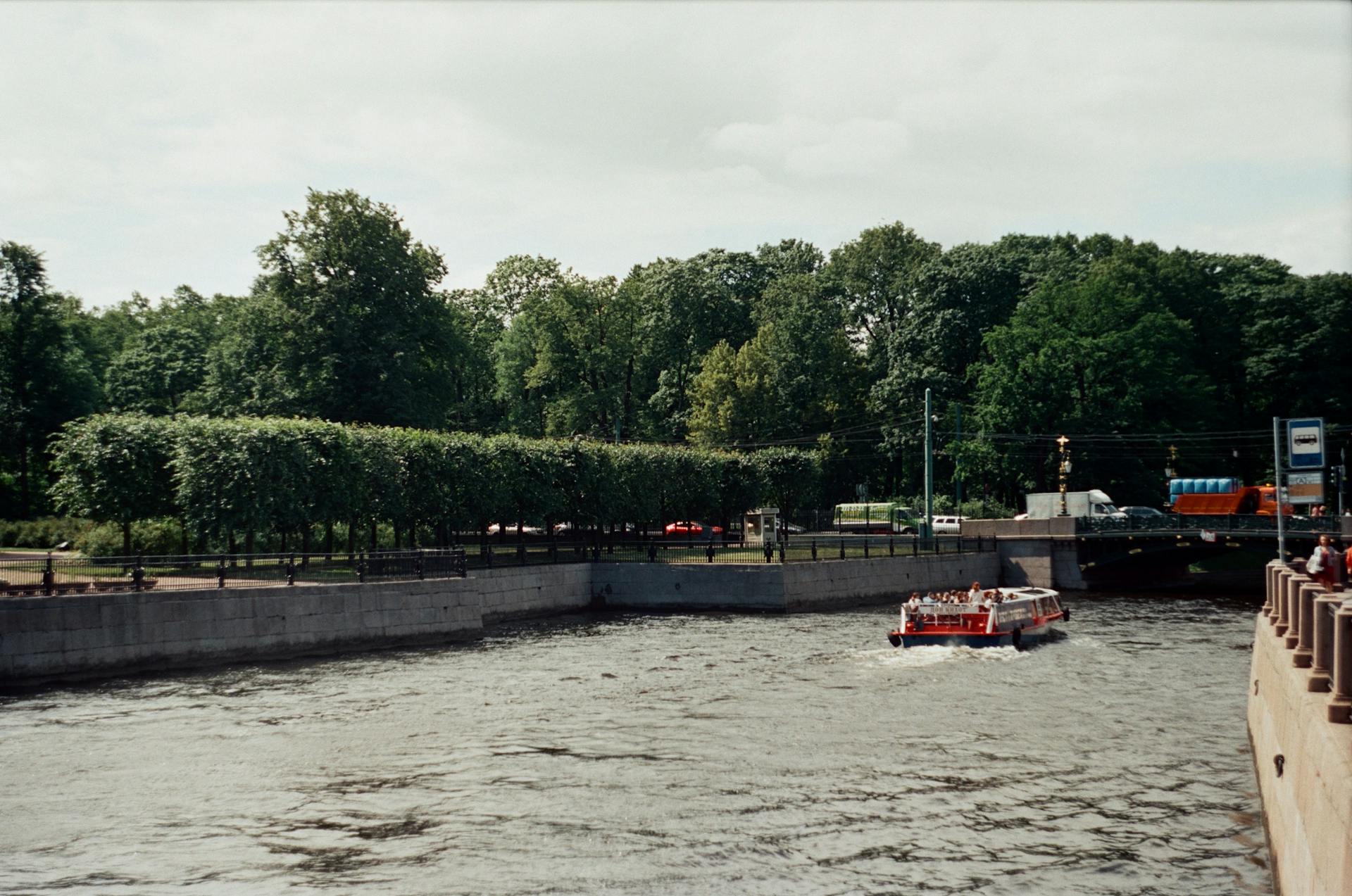 A calm river canal with a tour boat under a summer sky surrounded by lush greenery.