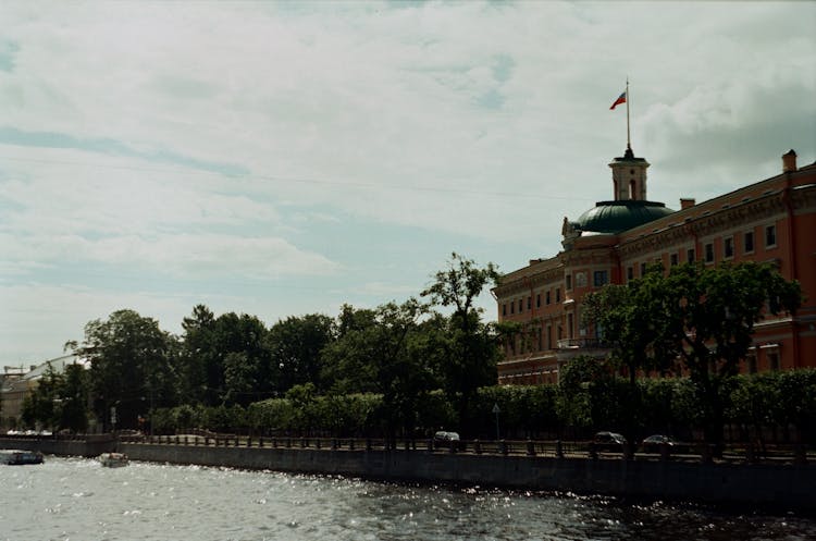 Mikhailovsky Castle With Flag On Top Beside Water In St Petersburg