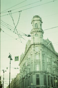 Vintage-style photo of a historic European building on a street corner with tram wires above.