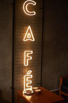 A cozy café interior featuring a neon sign and hot drinks on a wooden table.