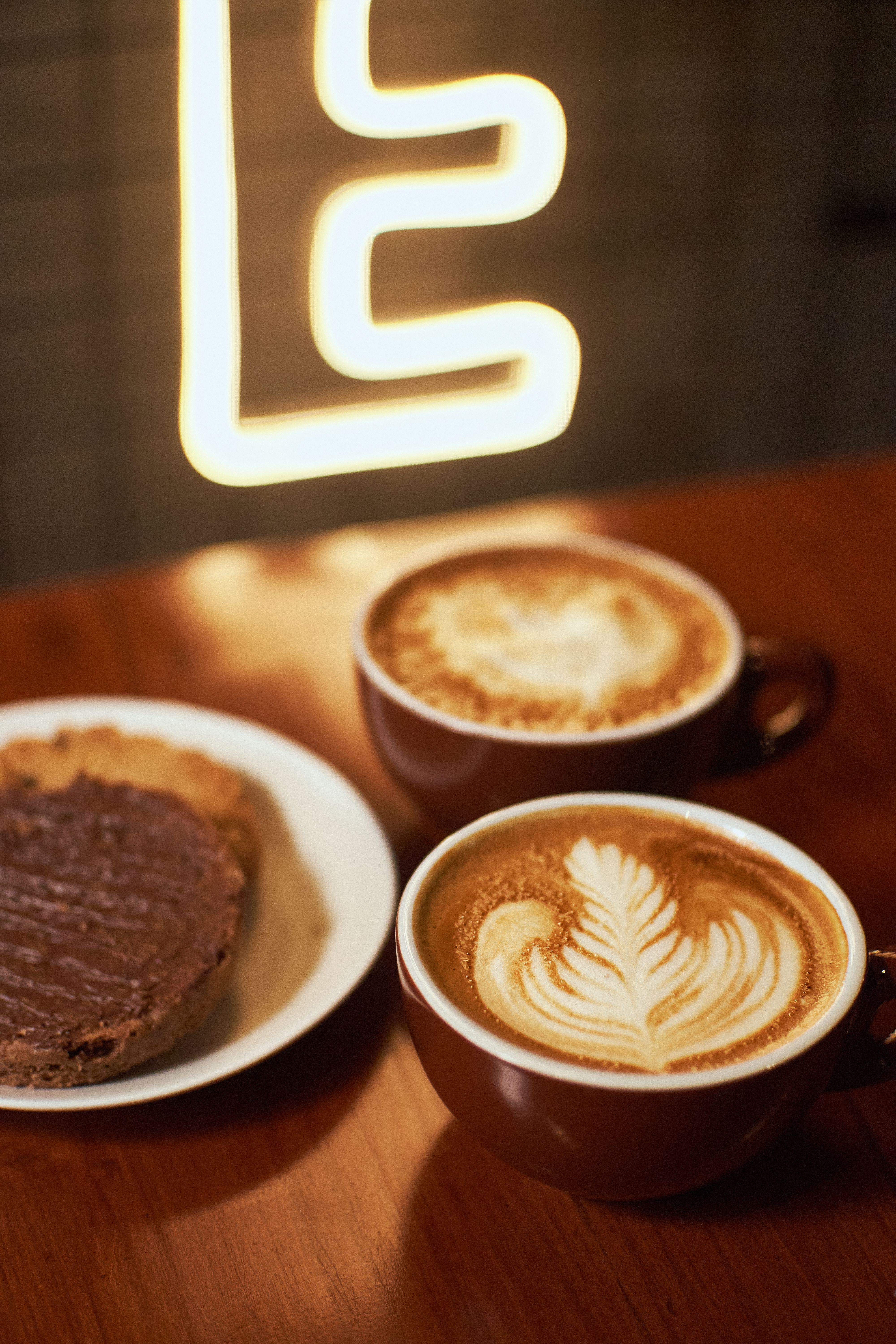 Close-up of elegant latte art and pastries on a wooden table in a cozy cafe setting.