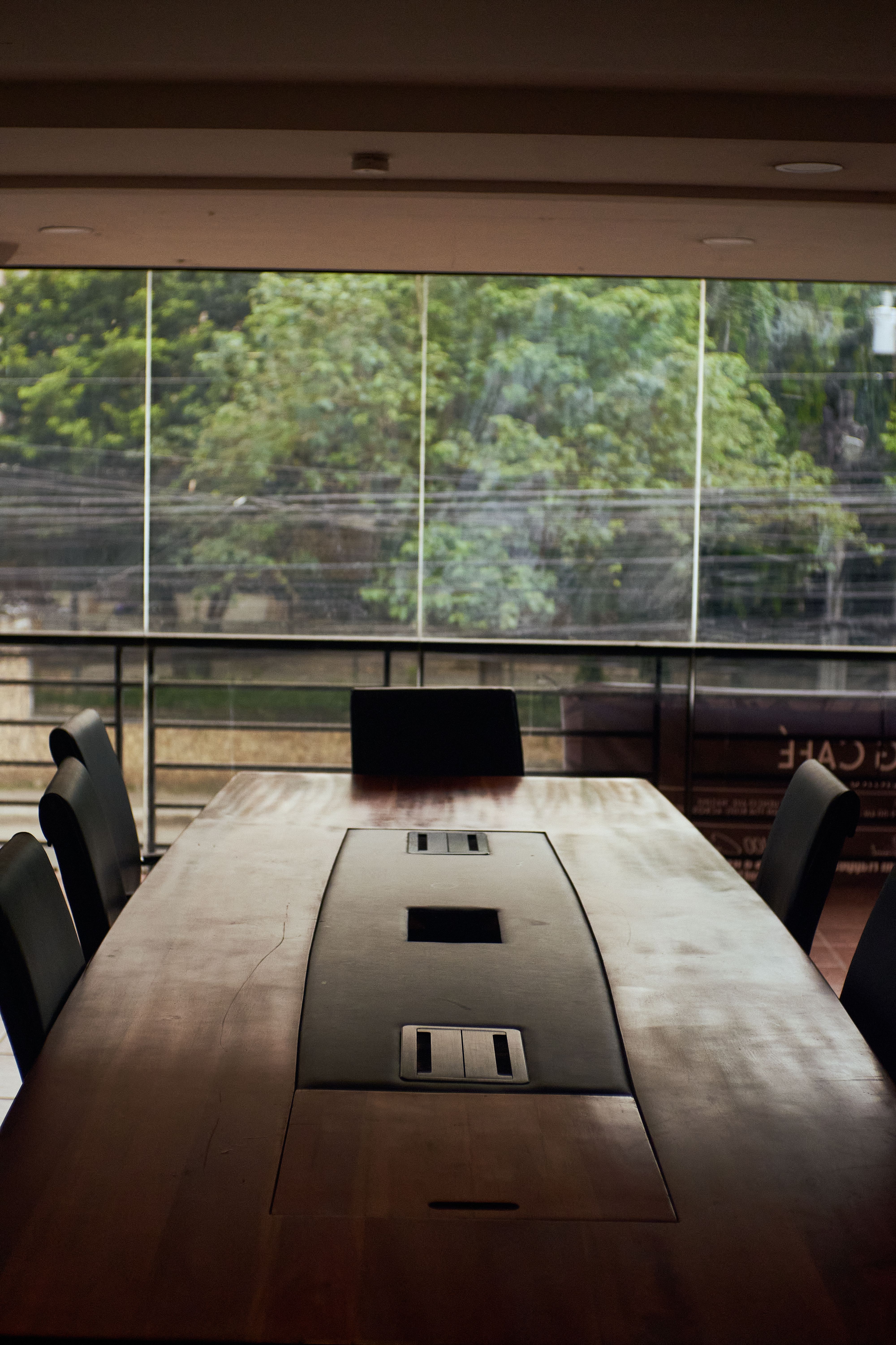 Spacious conference room with a wooden table, overlooking greenery through large windows.