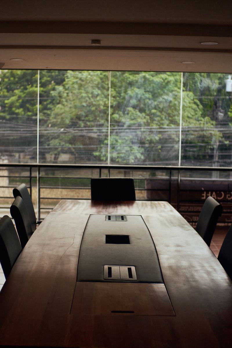 Spacious conference room with a wooden table, overlooking greenery through large windows.