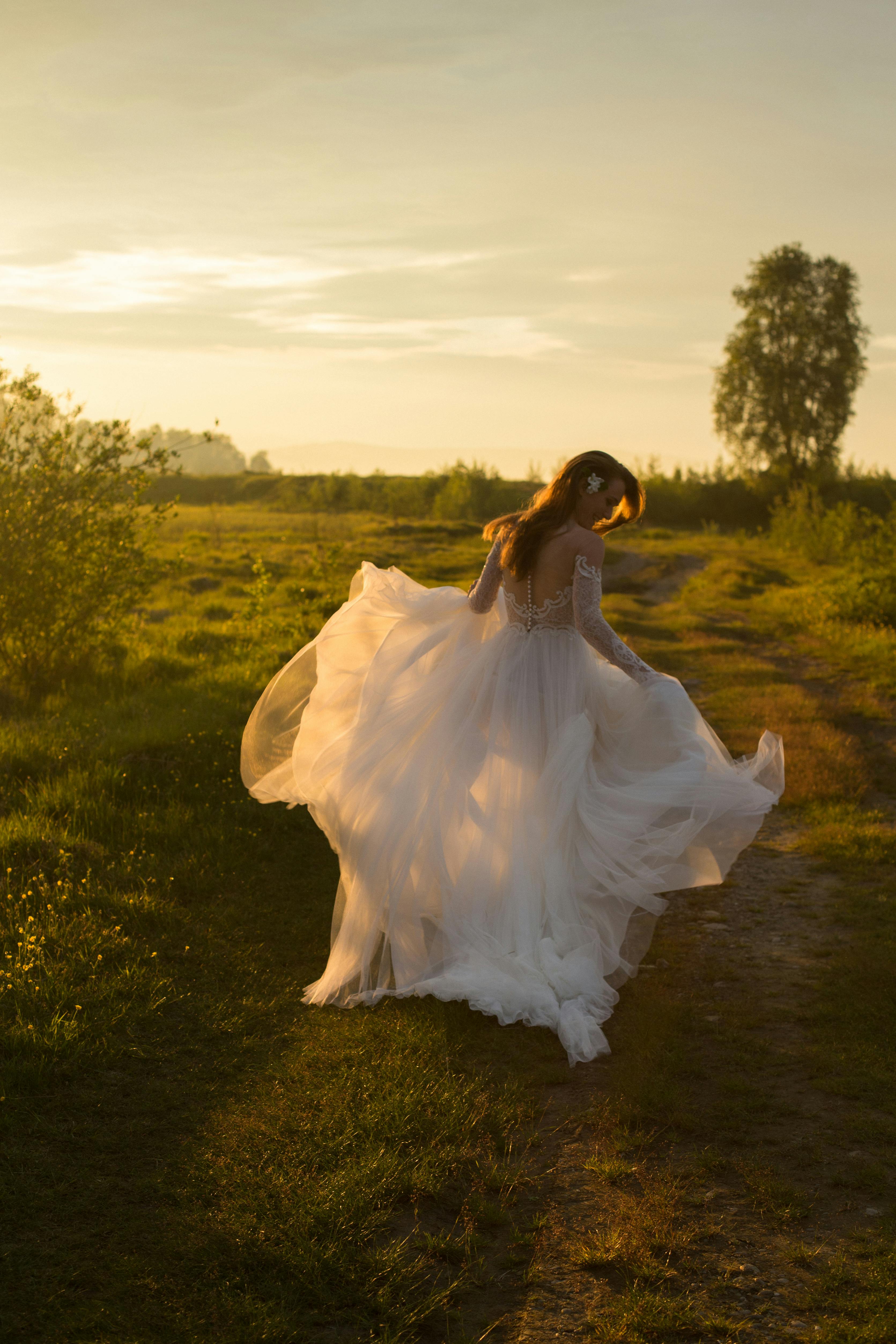 A bride walking in a wedding dress along a country path during a golden sunset in nature.