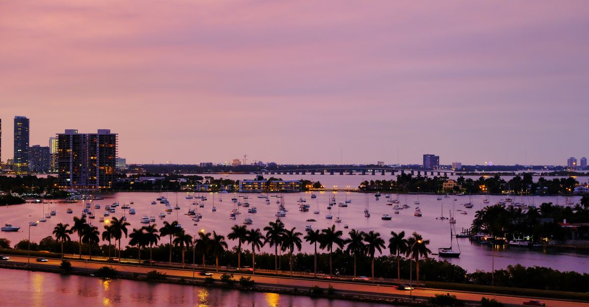 An aerial view of Miami's skyline at twilight, featuring water reflections and palm trees.