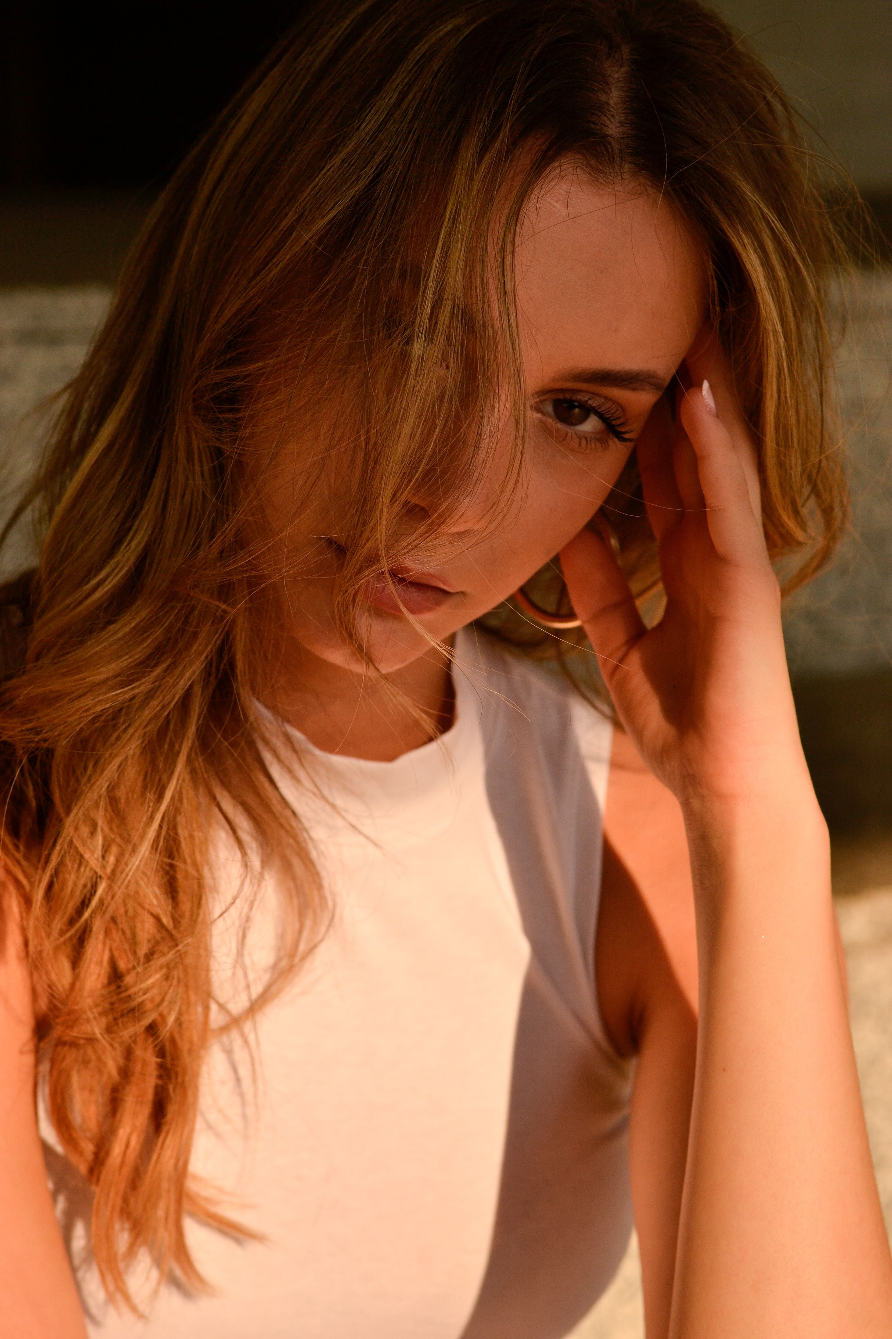 Close-up portrait of a woman in a white tank top, lit naturally with artistic shadows.