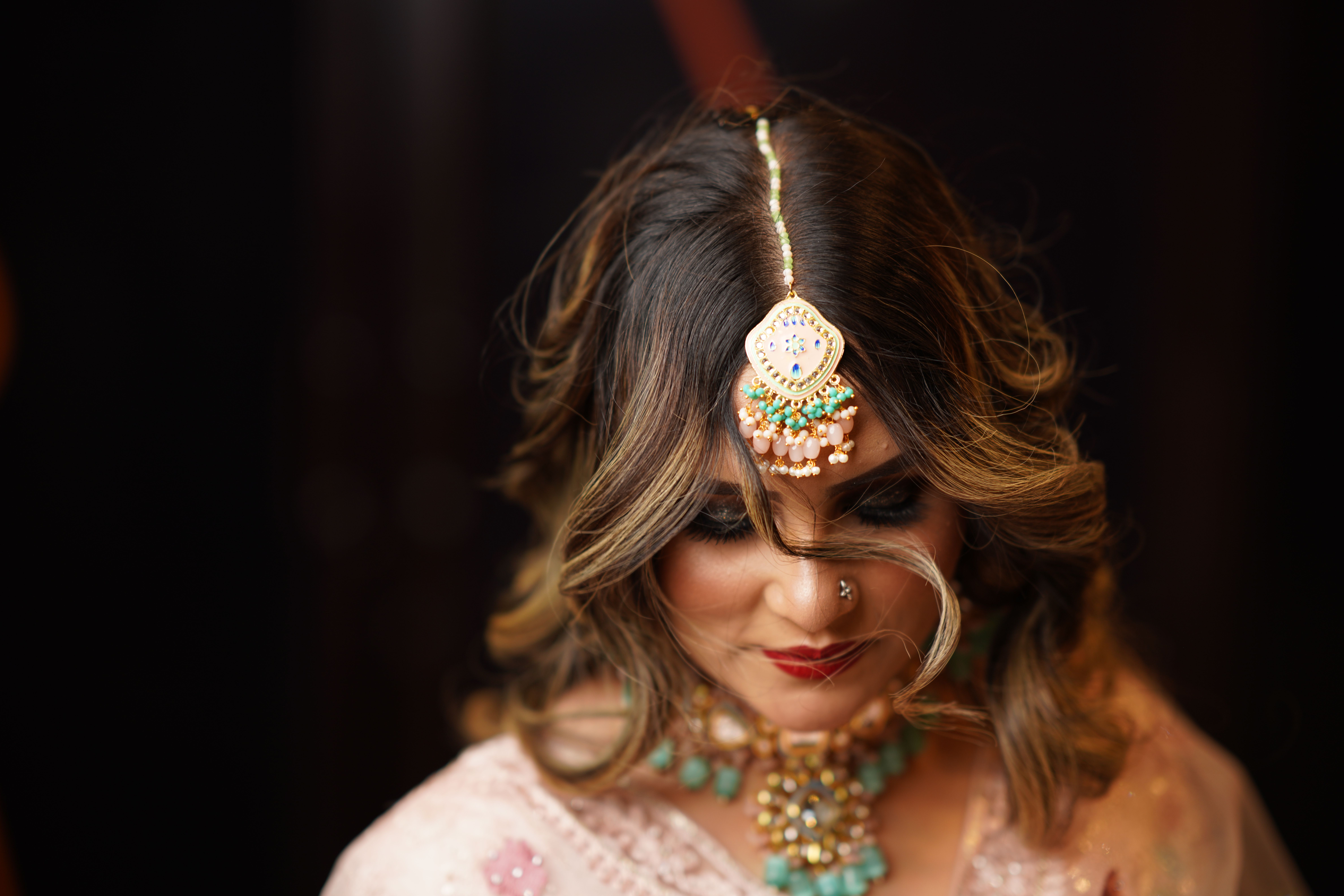 Close-up of Indian bride wearing traditional jewelry and maang tikka, exuding elegance.