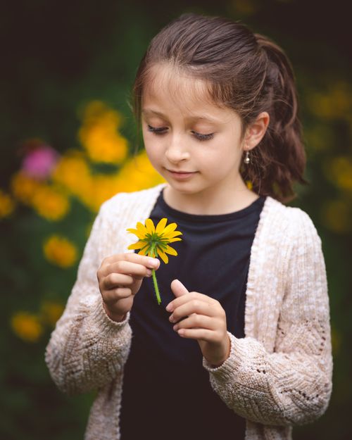 Free Portrait of a young girl holding a yellow flower outdoors, surrounded by vibrant spring blooms. Stock Photo