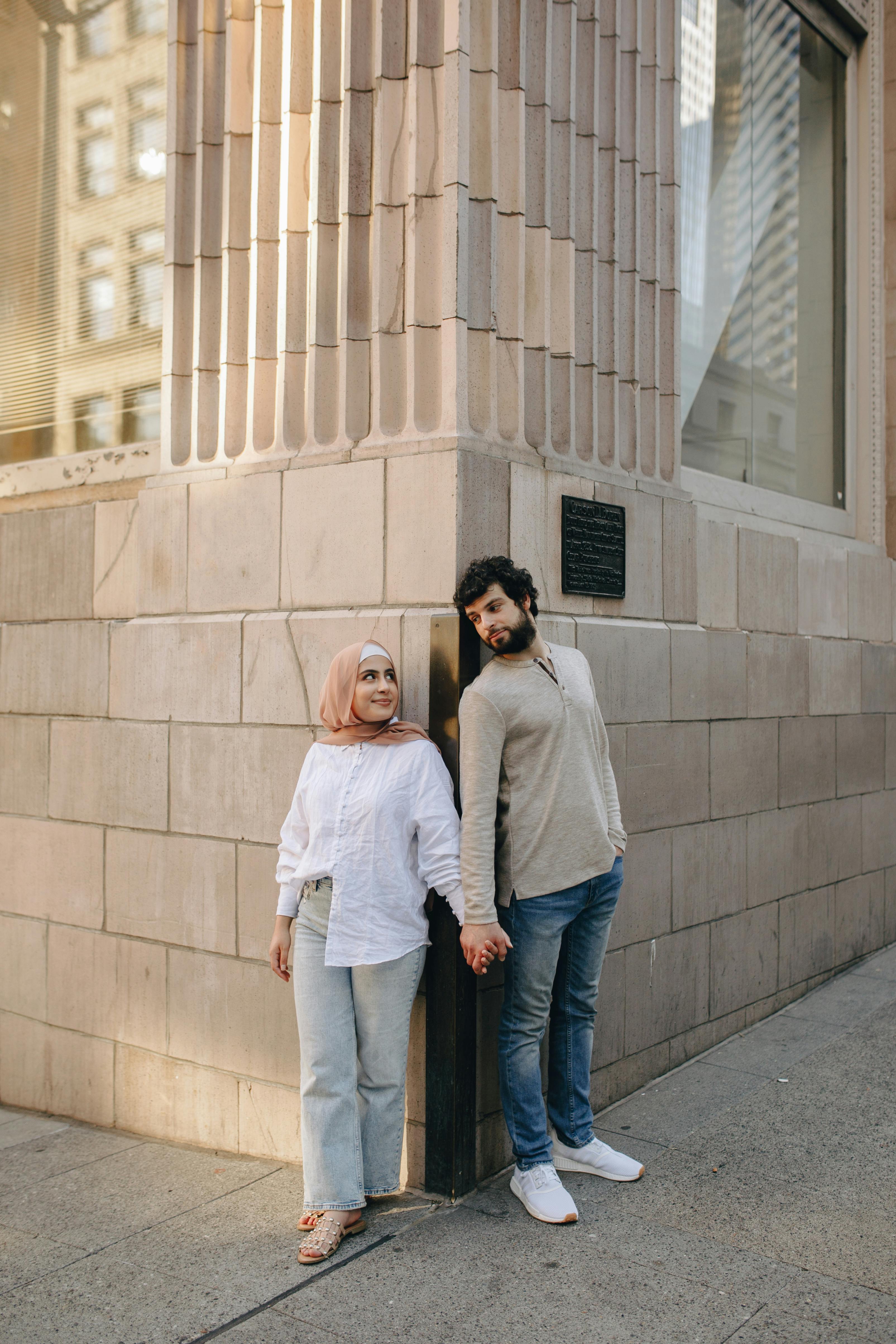 Free A romantic couple stands holding hands against a city building corner. Stock Photo