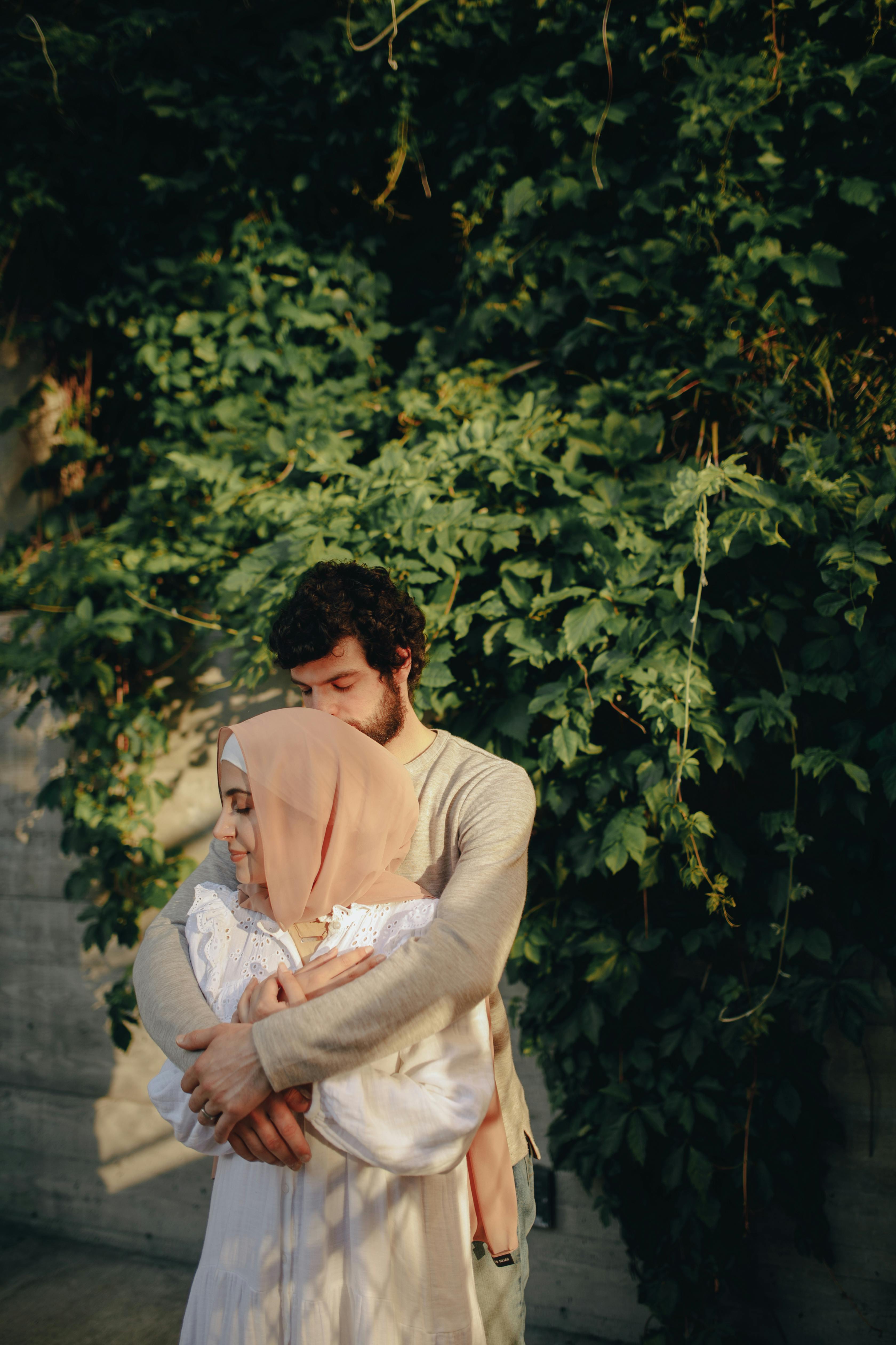 A loving couple embraces outdoors, surrounded by lush greenery and natural light.