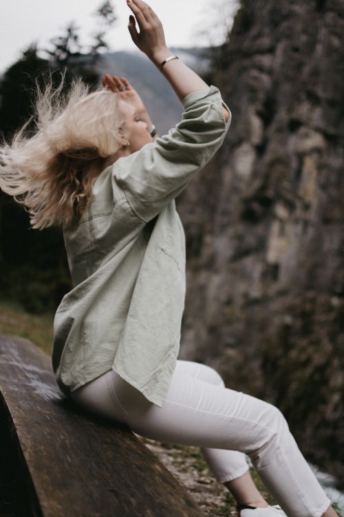 Free Blonde woman on edge of wooden bench with natural cliff backdrop, outdoors. Stock Photo