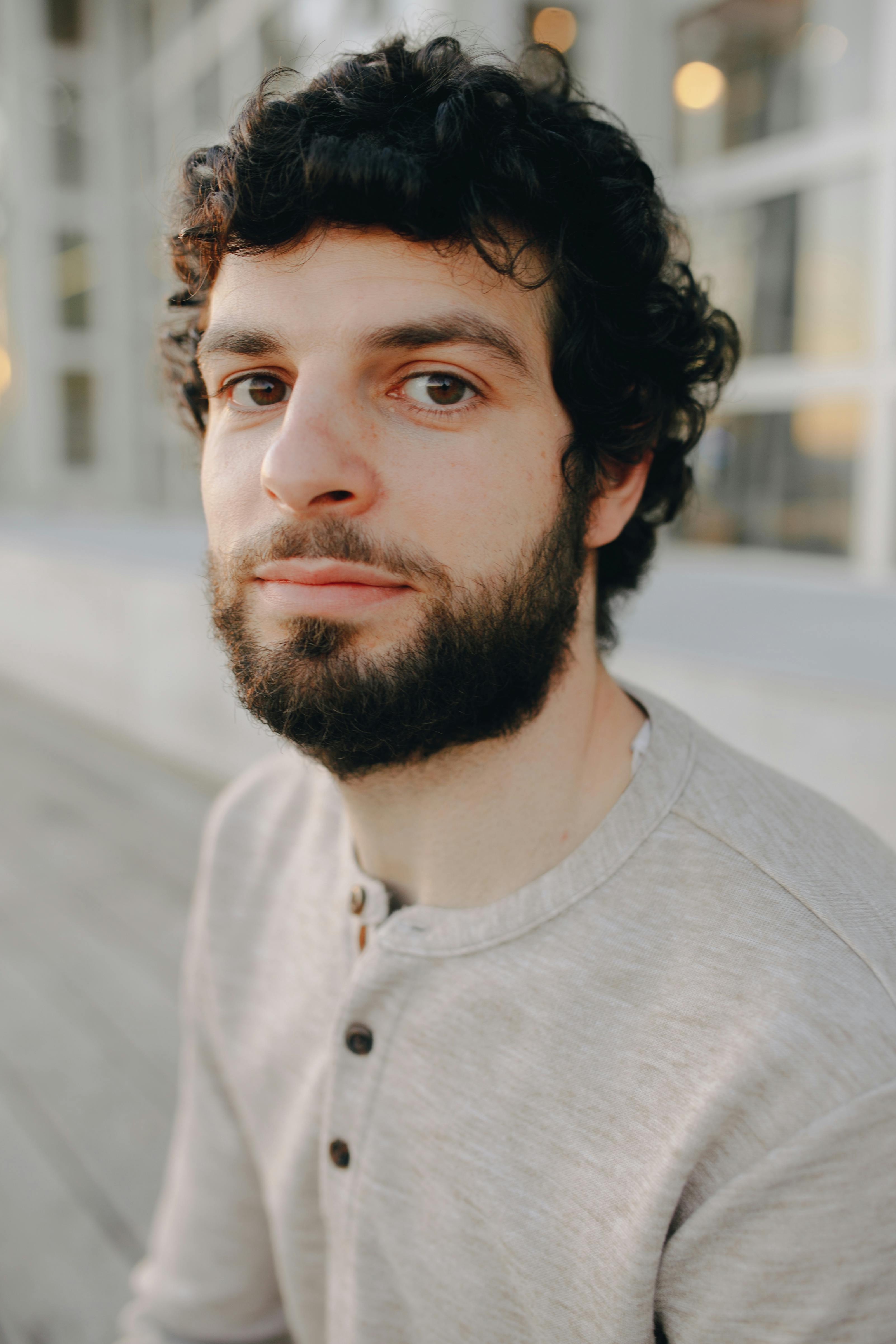 Casual outdoor portrait of a young bearded man with curly hair in natural light.