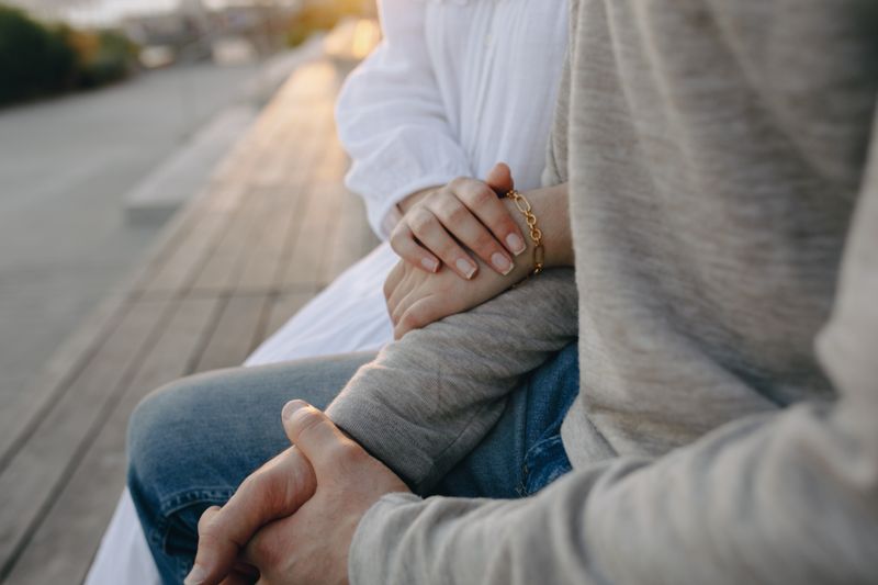 Close-up of two people holding hands on a bench, a natural gesture of connection and support