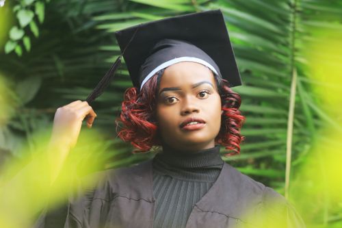 Free A confident graduate wearing a cap and gown standing against lush greenery, symbolizing educational success. Stock Photo