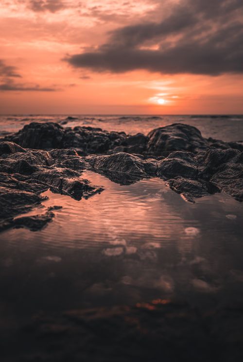 Free Stunning sunset view over a rocky shore with reflection on water, capturing nature's drama. Stock Photo