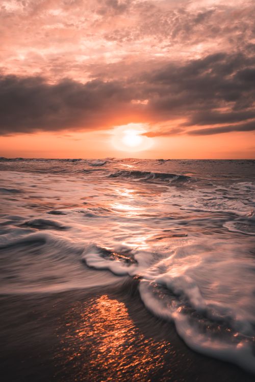 Free Captivating ocean waves crashing on the shore during a stunning sunset with vibrant colors. Stock Photo