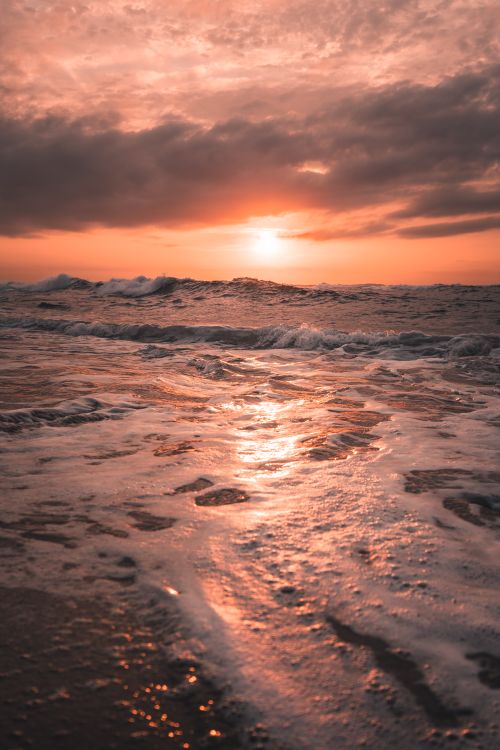 Free Sun setting over a tranquil ocean with waves gently rolling ashore, creating a picturesque and peaceful scene. Stock Photo