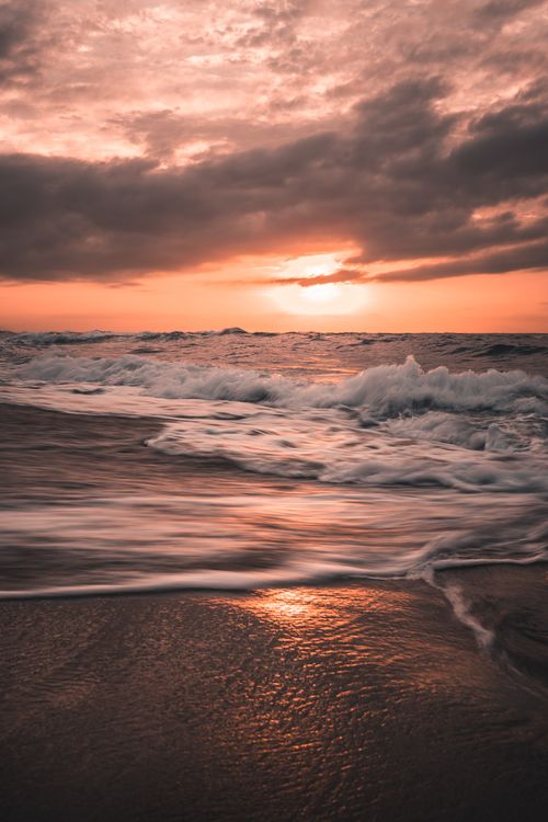 Free Captivating view of dramatic waves crashing at ocean shore during a stunning sunset. Stock Photo
