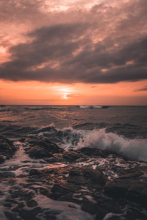 Free Capture of the ocean's waves crashing against rocks at sunset, creating a scenic view. Stock Photo