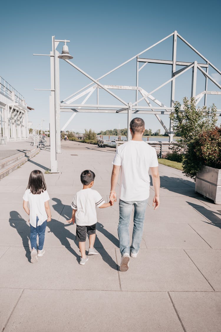 Back View Of A Family Holding Each Other's Hands While Walking On The Sidewalk