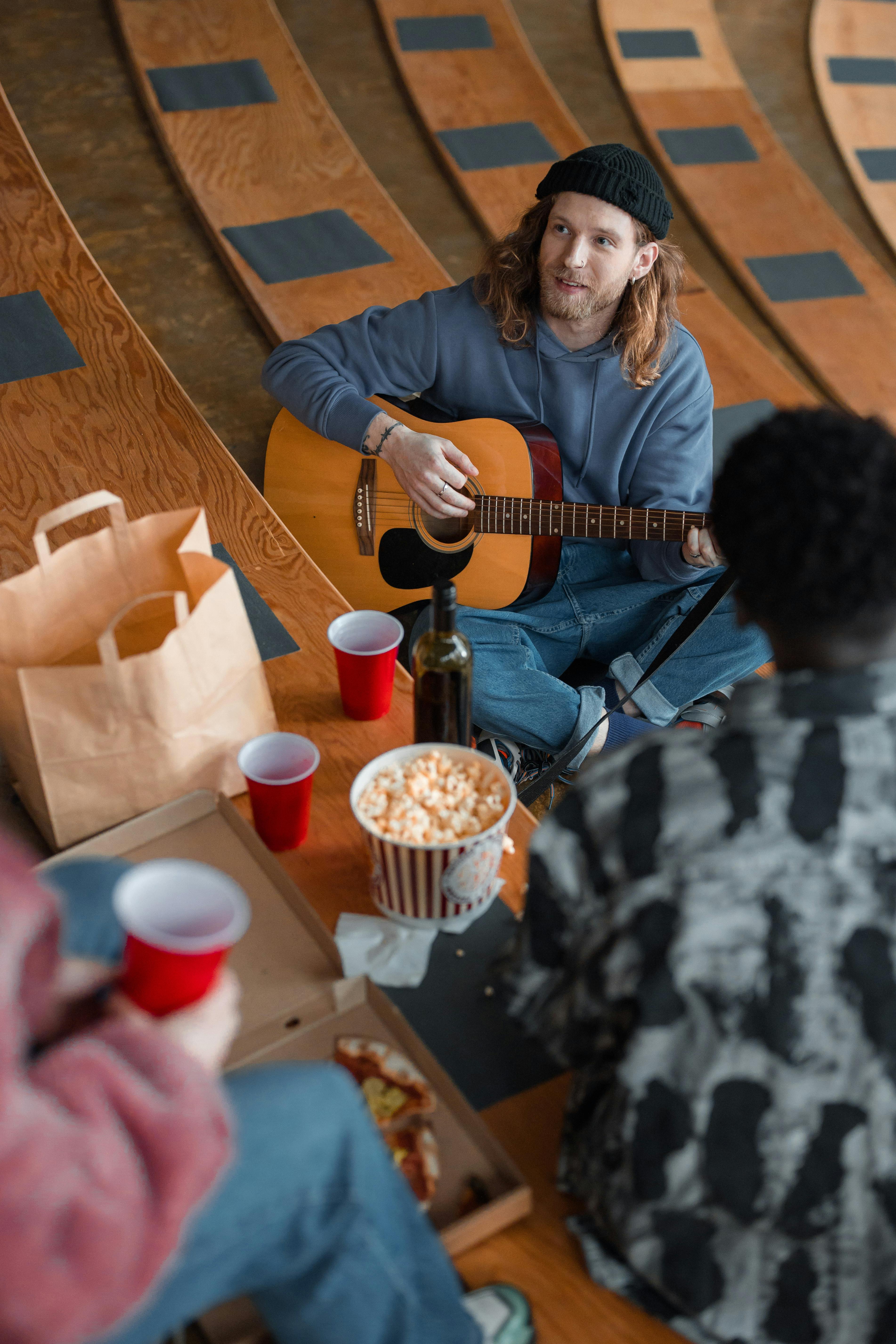 Free Group of friends having a picnic with guitar music, pizza, and popcorn in an amphitheater setting. Stock Photo