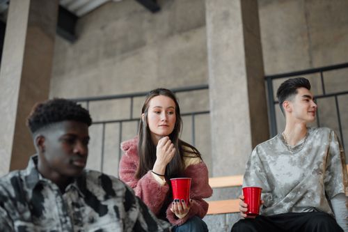 Free Three young adults enjoying a casual indoor gathering, chatting and holding drinks. Stock Photo