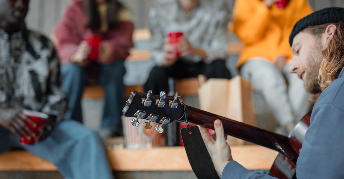 Casual gathering of friends enjoying acoustic guitar music at an outdoor venue.