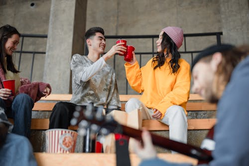 Woman in Yellow Long Sleeve Shirt Sitting beside a Man in Gray and White Long Sleeve Shirt Holding Red Plastic Cups