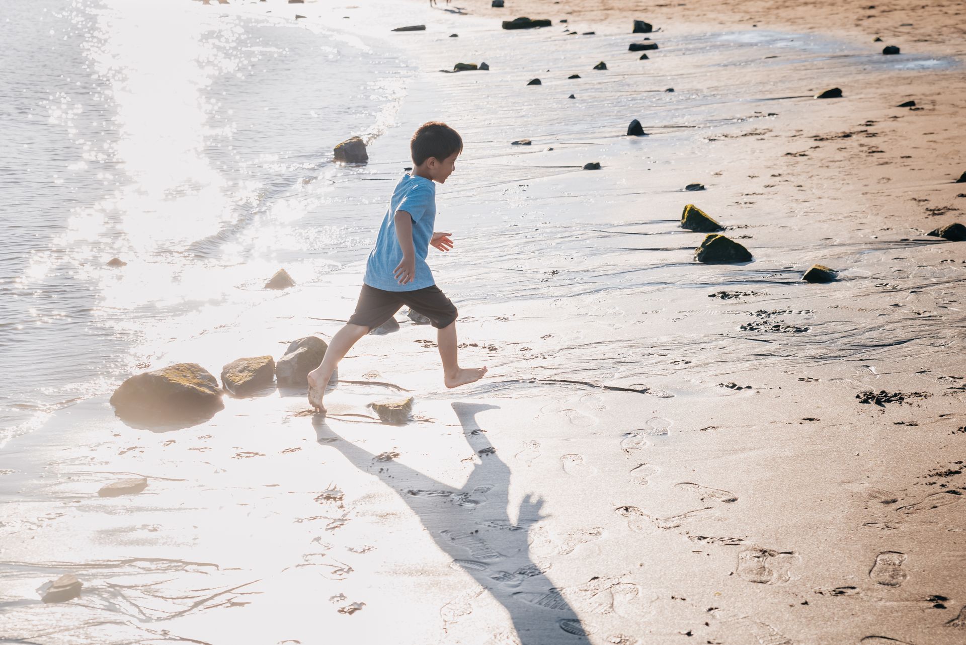 A child running barefoot along the shoreline at the beach, stepping over rocks at low tide