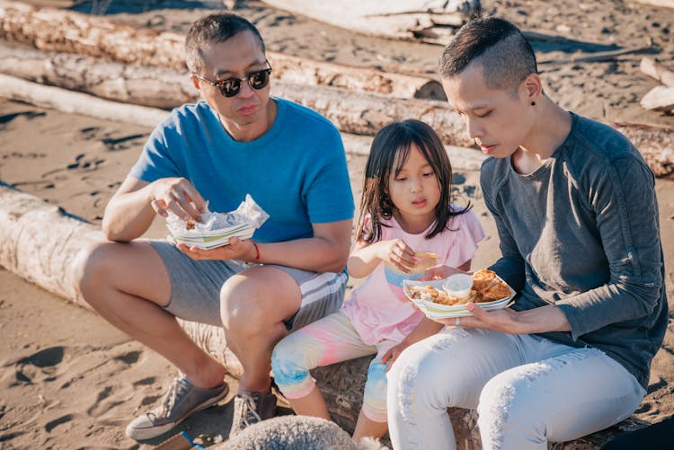 Family Sitting On A Log While Eating Snacks