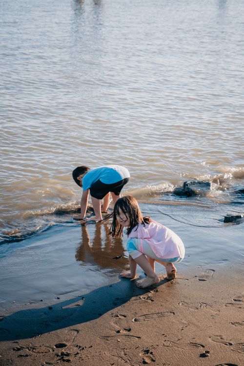 Free Kids play barefoot on a sunny beach, enjoying the water and sand. Stock Photo