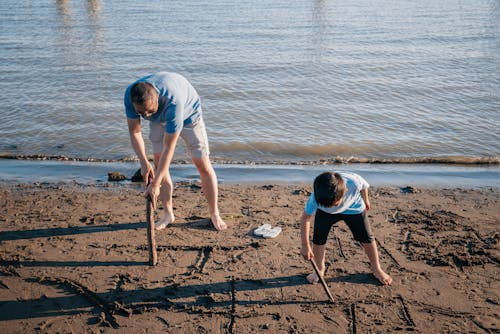 Dad and Son Writing on Beach Sand Using a Stick