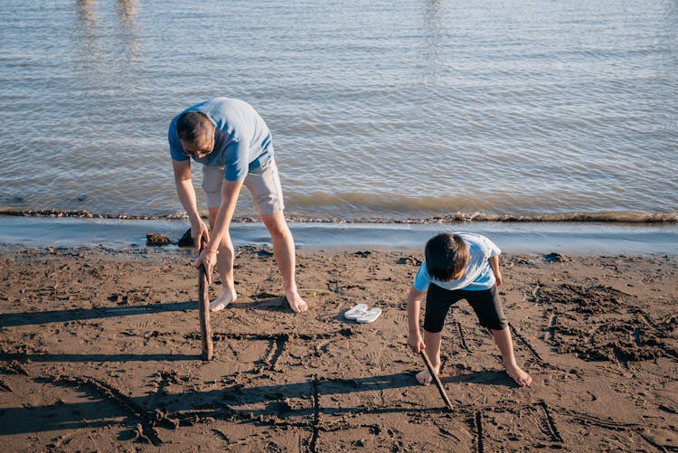 Dad And Son Writing On Beach Sand Using A Stick