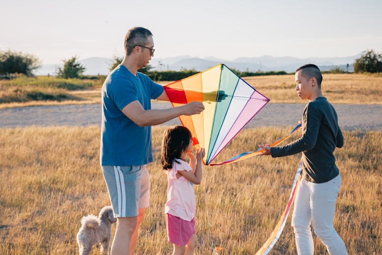 A Family Playing With Kite In The Grass Field