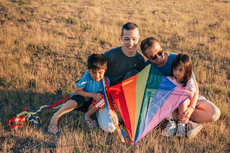 Happy Family Sitting On Grass While Holding A Colorful Kite