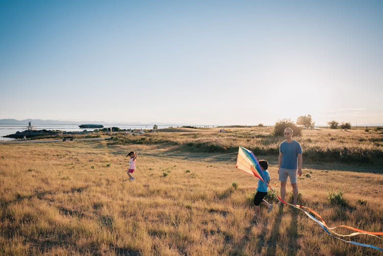 Happy Family Having Fun Playing With Kite On The Grass Field