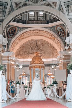 Bride in white gown walks down intricately designed church aisle for wedding.
