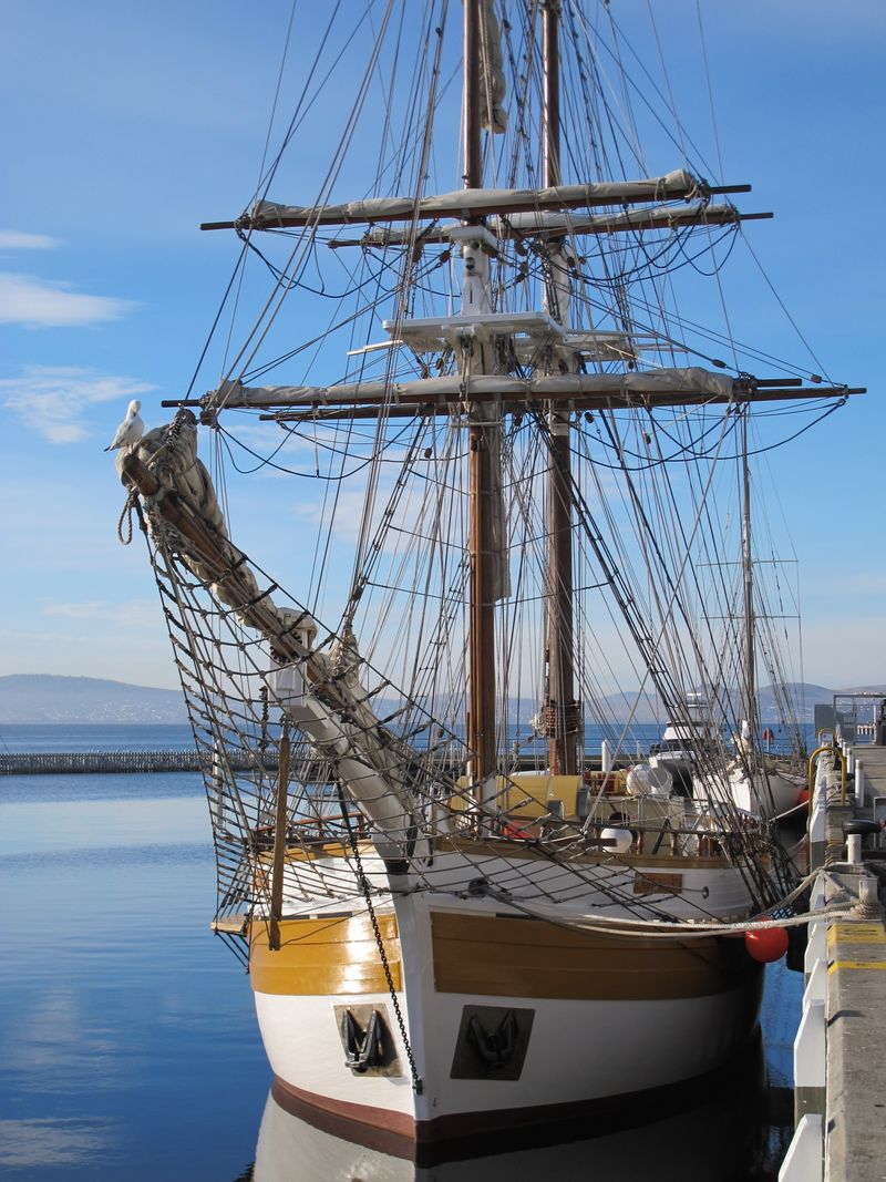 Historic sailing ship moored at a tranquil harbour under a clear blue sky