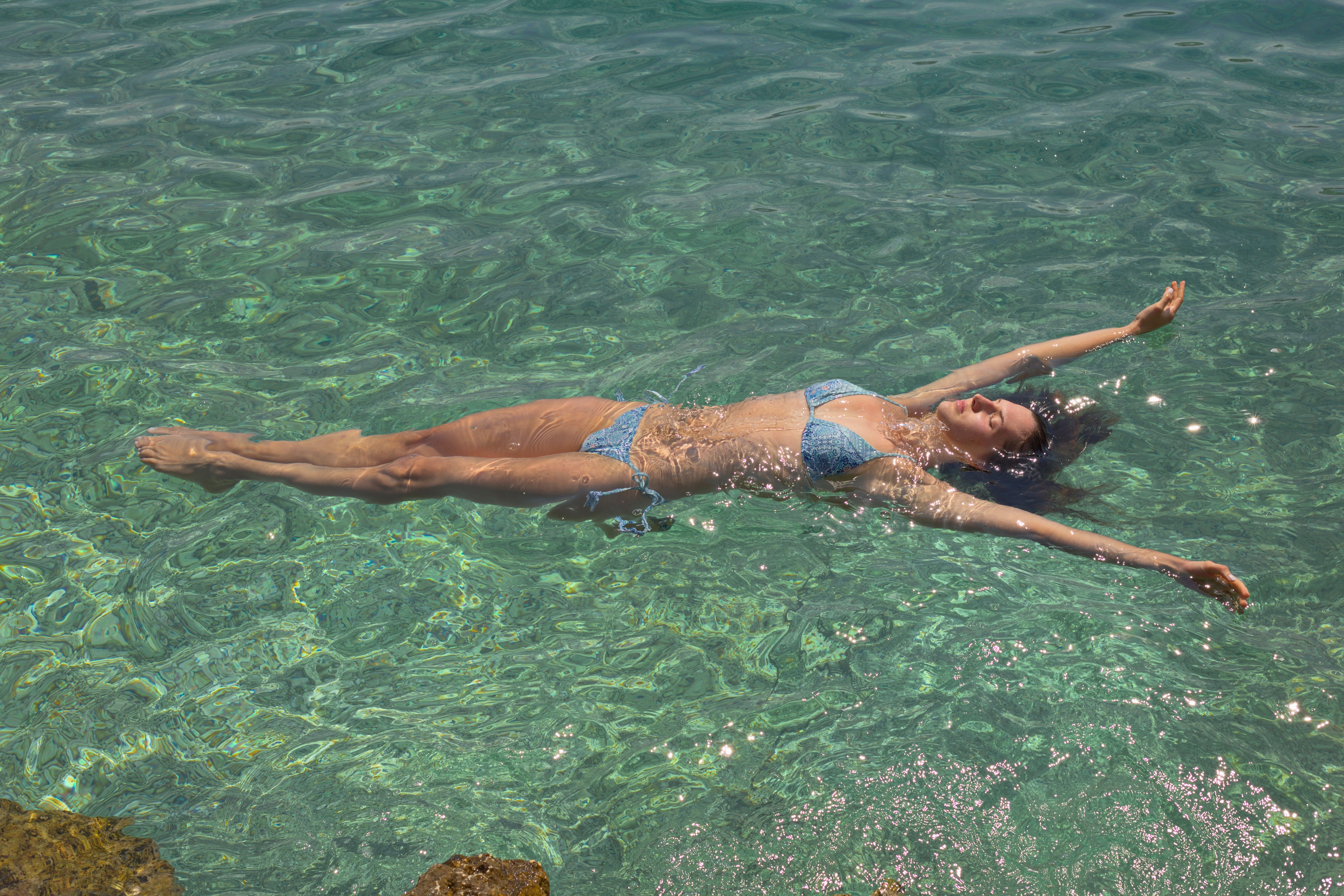 Young woman in bikini floating peacefully in clear turquoise sea on a sunny summer day.