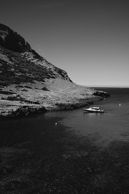 Free Grayscale Photo of Boat on Sea Near Mountain Stock Photo