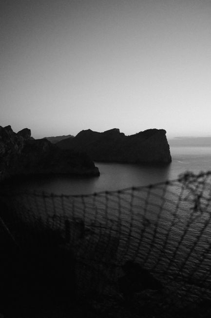 Striking black and white silhouette of rocky coastline in Pollensa, Spain, capturing the sea's timeless beauty.
