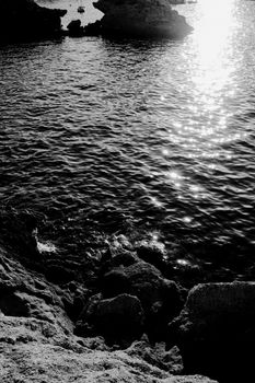 Sunlight reflecting on a tranquil rocky shoreline, creating a peaceful ocean scene.