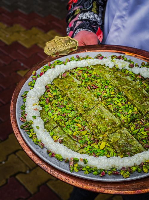 Free Close-up of a traditional pistachio-covered dessert served in an ornate platter, showcasing vibrant textures and colors. Stock Photo