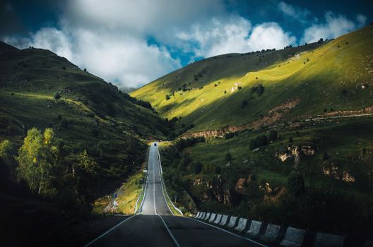 A stunning view of a road leading through lush green mountains under a sky of white clouds in Russia's Caucasus region.