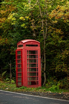 Classic red phone booth amidst vibrant autumn countryside foliage.