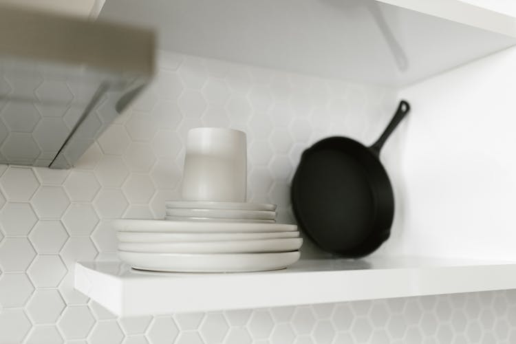 Stakced White Ceramic Plates On White Shelf 