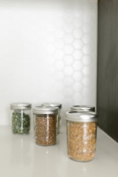 Neatly arranged glass jars filled with whole grains and spices on a white shelf.
