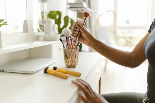 A woman organizing makeup brushes on a white dresser in a bright and modern room.